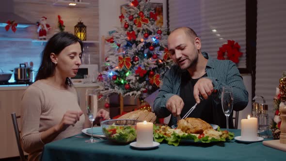 Man Cutting Chicken for Woman at Festive Dinner on Christmas Eve