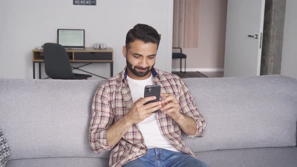 Young Attractive Indian Man Sitting on Sofa Holding Cellphone at Home