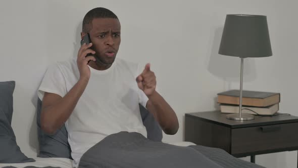 Angry African Man Talking on Smartphone in Bed