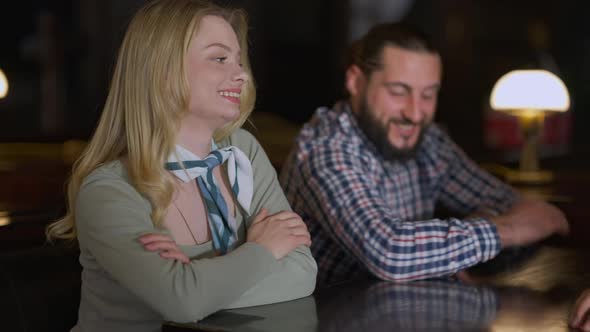 Charming Woman Sitting at Table with Friends Smiling Listening Stories