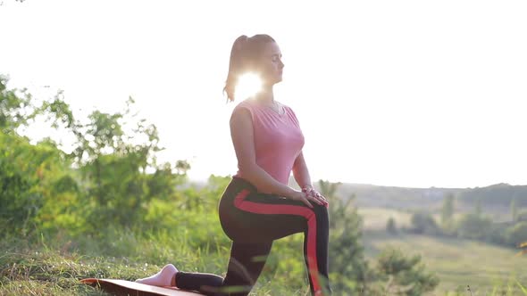 Side view of a meditating woman sitting in a lotus position against a beautiful landscape.