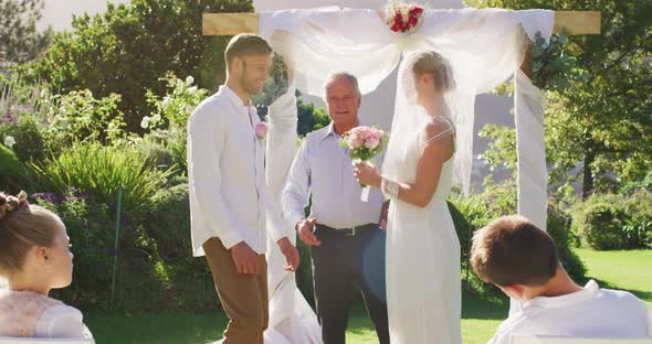 Caucasian bride and groom standing at outdoor altar with wedding officiant during ceremony