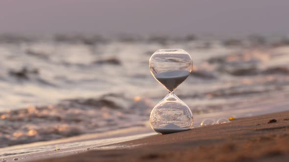 Hourglass stand on sand against wavy sea, selective focus