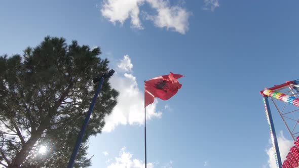 Proud Albanian Flag waving in the wind against the blue sky on top of flag pole