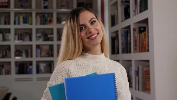 A Young Student Girl in the Library with Notebooks in Her Hands