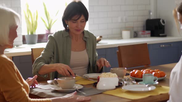 Concentrated mature women cuts cake and drinking tea