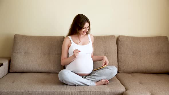 Pregnant Woman Applying Headphones in the Sofa. Expectant Mother Listening Music and Dancing in