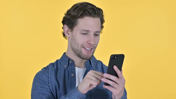 Portrait of Young Man Using Smartphone on Yellow Background