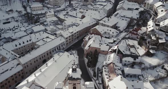 Flying above Christian Church and rooftops covered by snow in Mining town Banska Stiavnica, Aerial s