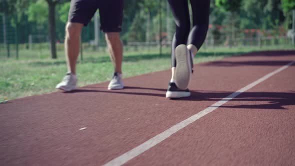 Legs of Unrecognizable Fit Man and Woman Running on Sunny Track Outdoors. Sportive Caucasian Couple