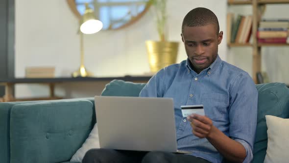 Online Shopping Success on Laptop By Young African Man on Sofa