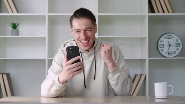 Surprised Man Winner Hold Smartphone Read Good News Amazed By Mobile Online Bet Bid Game Win at Home