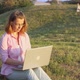 A young woman works on a laptop remotely while sitting in a park in nature in the summer. - VideoHive Item for Sale