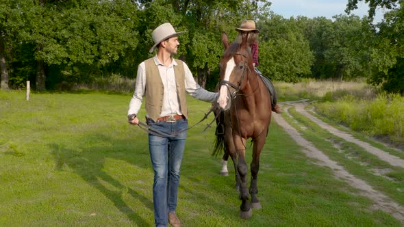 A Young Cowboy is Leading a Horse on Which His Daughter is Sitting