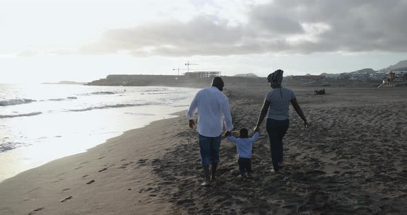 Happy african couple walking on the beach with little son