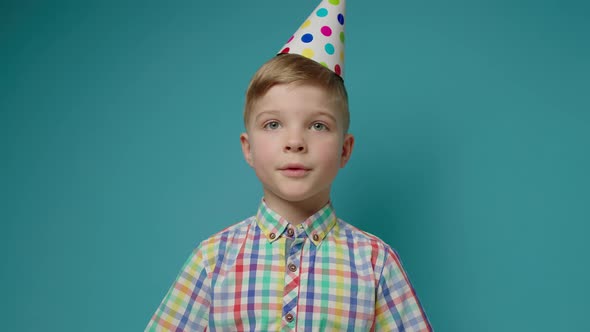 Cute Young Boy Wearing Birthday Hat Talking to Camera on Blue Background