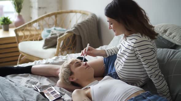 Lesbian Young Woman are Doing Makeup and Kissing Lying on Bed in Modern Apartment Spbd