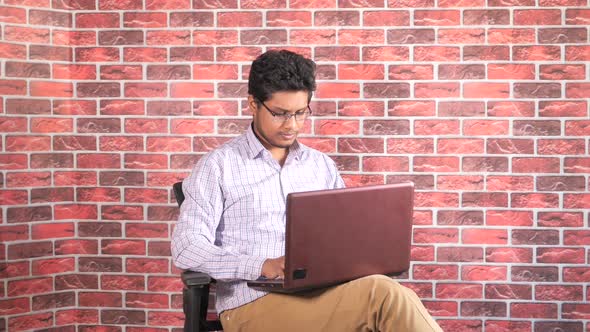 Young Man Sitting on Chair Typing on His Laptop 