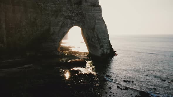 Drone Flying Along Epic White Cliffs of Normandy Shore Towards Natural Backlit Rock Arch 