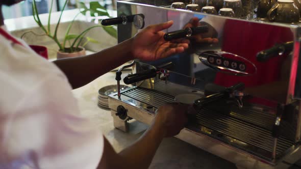 Midsection of african american male barista making coffee in coffee machine