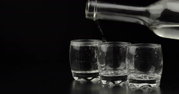 Pouring Up Three Shots of Vodka From a Bottle Into Glass. Black Background