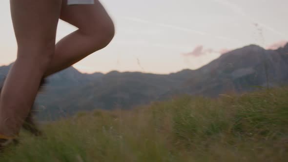 Close up shot of woman legs hiking on field against mountain hill slow motion.
