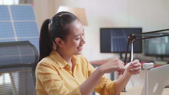 Close Up Of Asian Woman Sits In Front Of Solar Cell Looking At Propeller Of Wind Turbine While Work