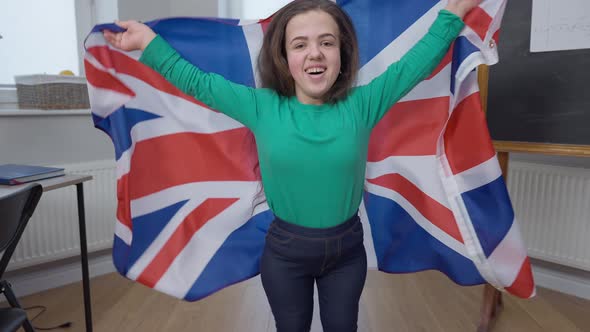 Portrait of Joyful Little Person Jumping with British Flag Looking at Camera Smiling