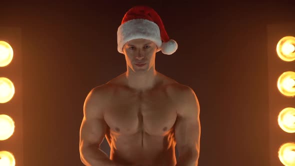 Portrait of Muscular Man Wearing Christmas Santa Hat Folded Hands on Smoky Background