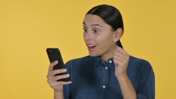 Latin Woman Celebrating on Smartphone Yellow Background