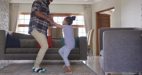 Happy african american daughter and father having fun, dancing in living room