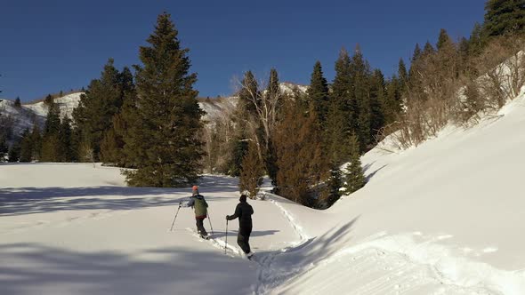 Panning aerial view of couple snowshoeing through new snow