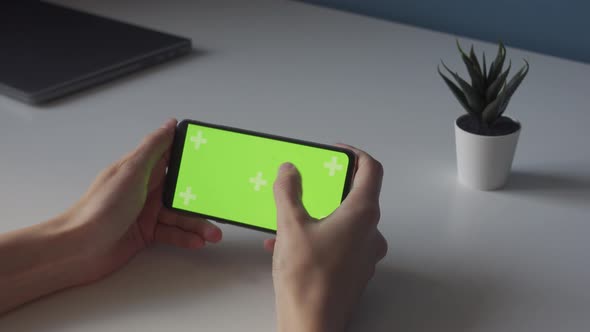 Horizontal Chroma Key Green Screen on Smartphone in Thin Hands on White Table