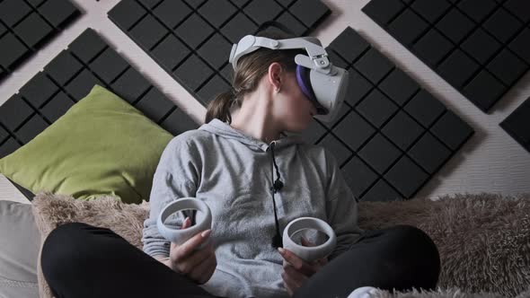 Young Woman in Virtual Reality Helmet Sitting on Sofa and Move Hands at Home