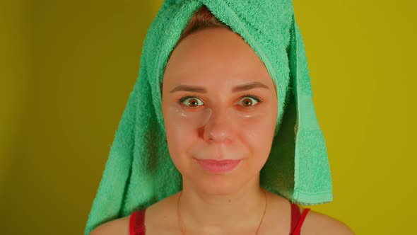 Woman with Towel on Head and Patches Under Her Eyes Smiles Looking at Camera