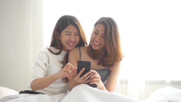 young asian women LGBT lesbian happy couple sitting on bed hug and using phone .