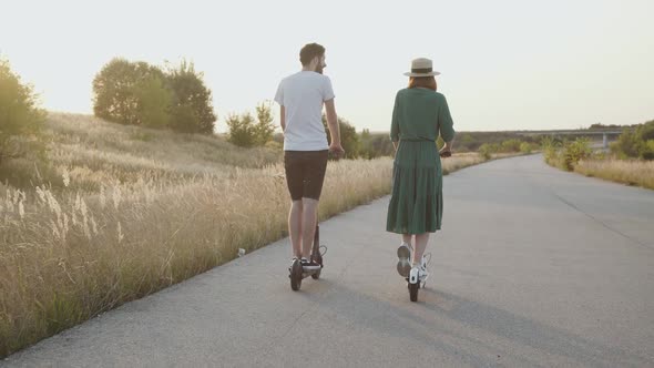 Couple in Love Riding to Sunset Together on Electric Scooters on Asphalt Road