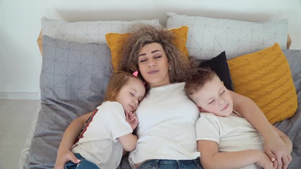 Mom and Daughter and Son Lie in Bed Together Hugging