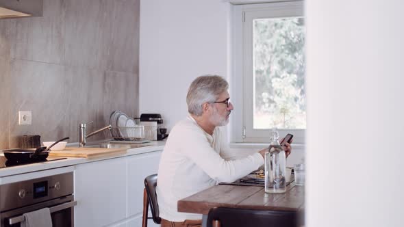 Mature man using smartphone at breakfast table