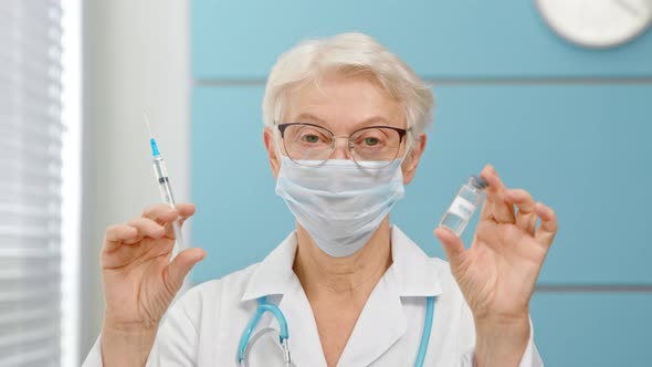 Skilled lady doctor with glasses and surgical mask shows vial of vaccine