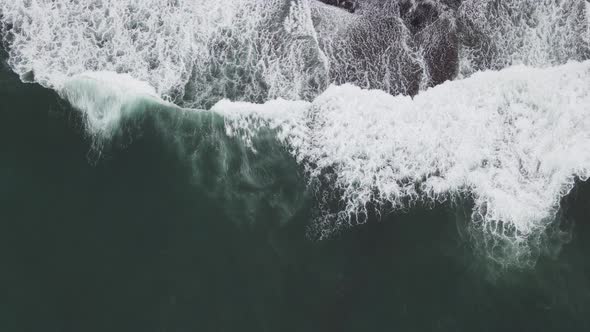 Top down aerial view of giant ocean waves crashing and foaming in coral beach