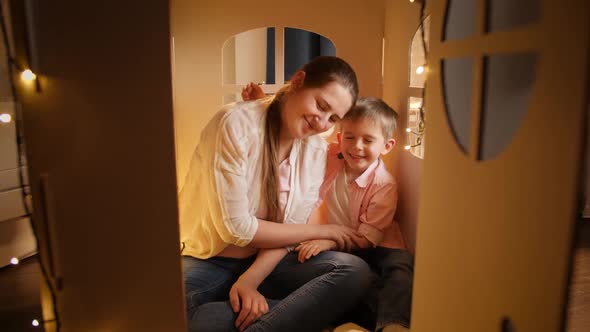 Happy Smiling Boy Huging and Embracing His Young Mother in Small Toy Huse or Tent at Night