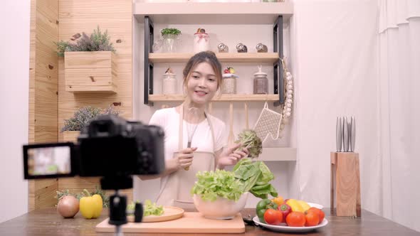 Asian blogger woman making salad in kitchen feeling happy dancing and sing a song cooking.