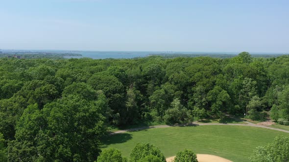 An aerial view above green tree tops in a park on a sunny day. The drone camera, focused on a bay in