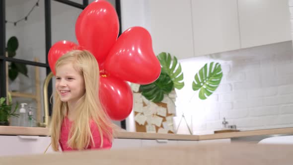 Little Blonde Girl Running Around the Table with Red Heart Shape Balloons at Home