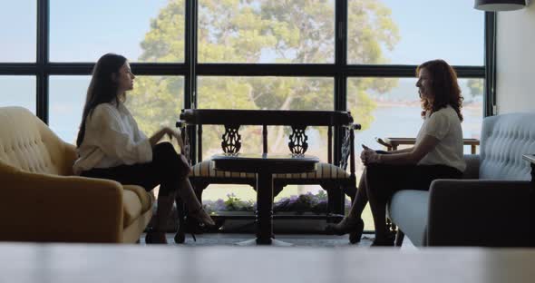 Two young businesswomen having a meeting in a beautiful hotel lobby with a view.