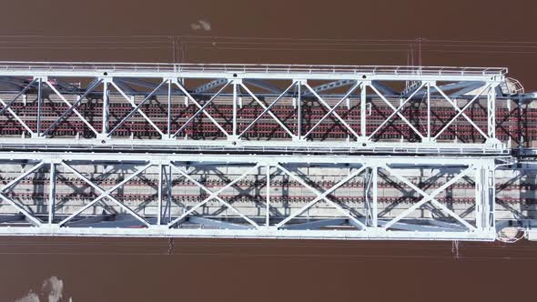 Aerial top down view of a railway bridge across a peat lake with light brown water and ice remnants.