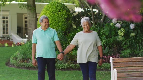 Video of happy biracial senior couple holding hands in garden