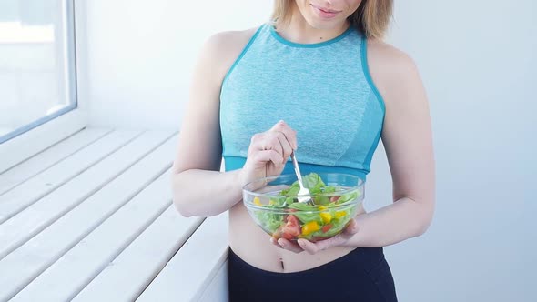 Happy Woman Eating Healthy Green Salad After Workout in a White Interior