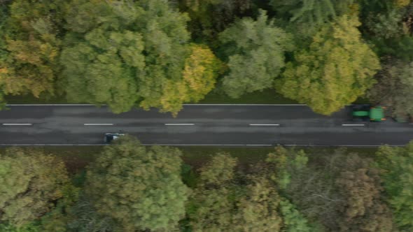 Coming in aerial shot of a car which is driving fast over a autumn colored street in a forest with o